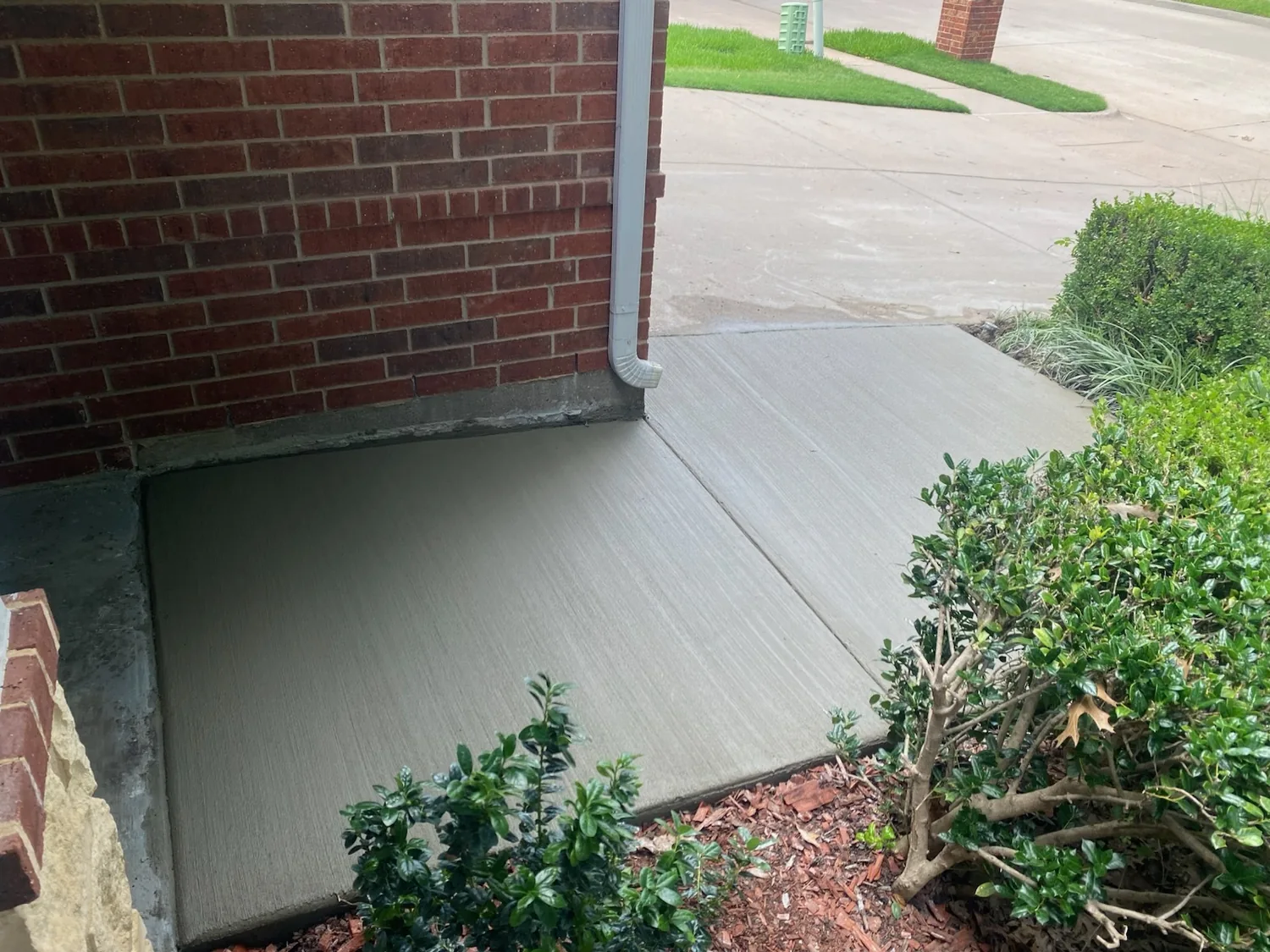 Fresh broom-finish residential concrete sidewalk wrapping a brick home corner by Lucky's Concrete